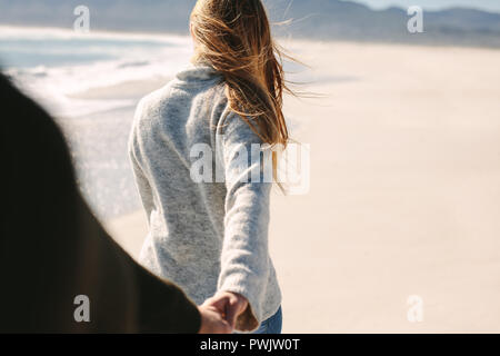 Woman holding boyfriend's hand while walking on the beach. Young couple walking along the beach. POV of man following girlfriend walking. Stock Photo