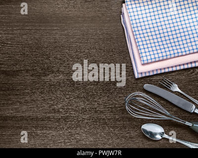 Fork, knife, spoon, whisk, kitchen towels lie on a wooden background horizontally with copy-space Stock Photo