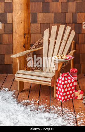 Adirondack chair with Christmas gifts and cookies on the snowy front porch of a rustic country cabin. Winter holiday vacation home getaways retreats. Stock Photo