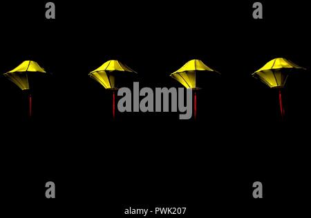 Row of four hanging yellow silk lanterns isolated against a dark background with space for copy Stock Photo