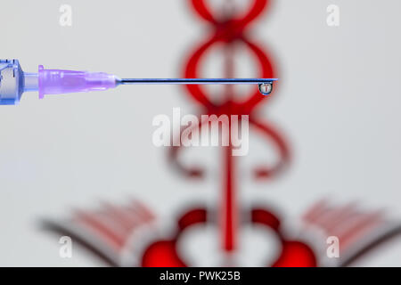 A droplet of vaccine at the tip of the needle and syringe reflecting red Caduceus symbol Stock Photo
