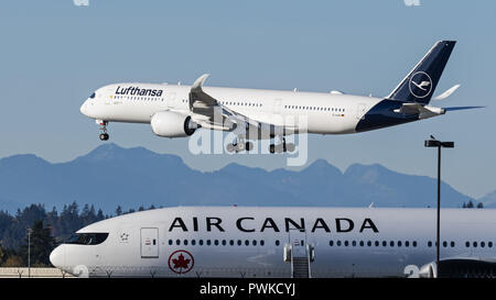 Richmond, British Columbia, Canada. 16th Oct, 2018. An Lufthansa Airbus A350-900 (D-AIXK) extra wide body (XWB) jet airliner airborne on short final approach for landing passes by an Air Canada Boeing 777-300ER jetliner parked on the tarmac at Vancouver International Airport. Credit: Bayne Stanley/ZUMA Wire/Alamy Live News Stock Photo