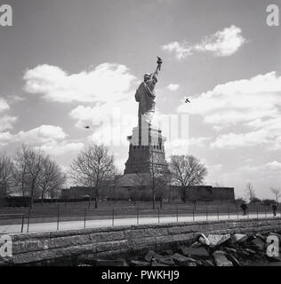 1950s, historical, view from behind of the statue of liberty on Liberty island in New York harbour, a neoclassical, copper built sculpture, a gift from the peoples of France to the USA to celebrates their alliance in the American revoloution.. In the distance we see a helicppter up close to the monument. Stock Photo