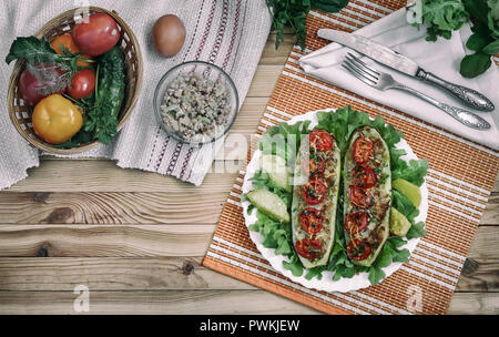 Zucchini on a plate stuffed with minced meat and vegetables with potatoes and green salad. Next to them Stock Photo