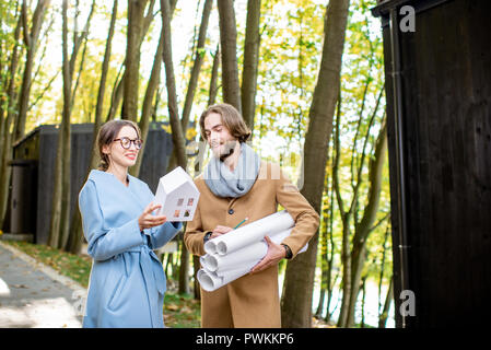 Creative couple of architects or designers standing with drawings and house model outdoors in the forest Stock Photo