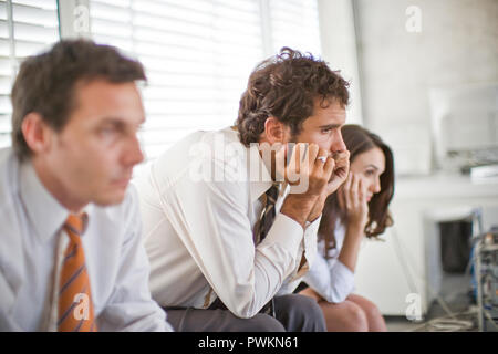 Young business man sitting in between two colleagues with his chin in his hands in an office. Stock Photo
