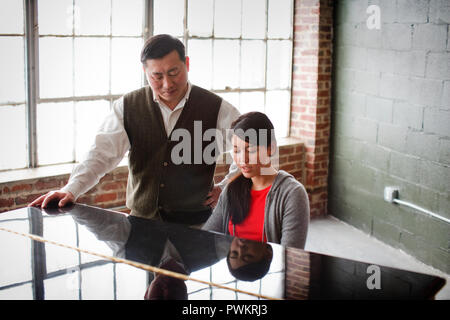 Daughter playing piano while her father stands nearby and watches. Stock Photo