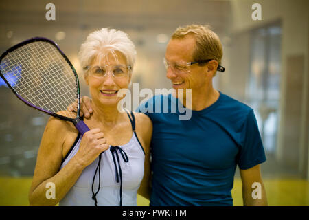 Portrait of a smiling senior woman holding a squash racket while standing with her playing partner. Stock Photo