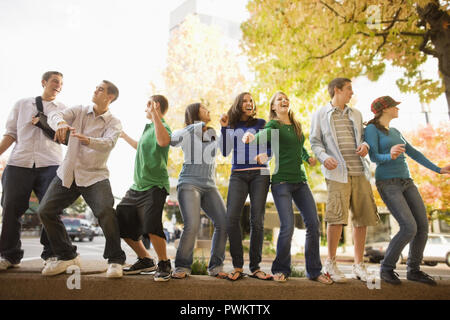 Group of teenagers dancing and having fun on top of a stone wall in the street. Stock Photo