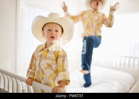 Portrait of a young boy wearing a hat while standing on a bed with his older brother. Stock Photo