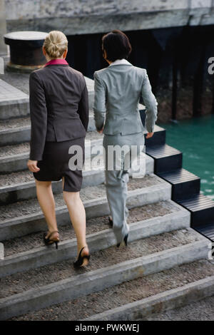 Two businesswomen walking together up a flight of cement steps on a wharf. Stock Photo