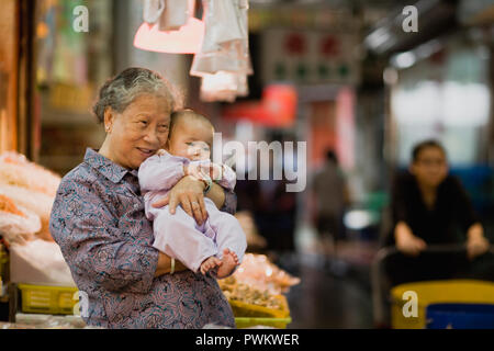 Grandmother holding a young baby inside a marketplace in the city. Stock Photo