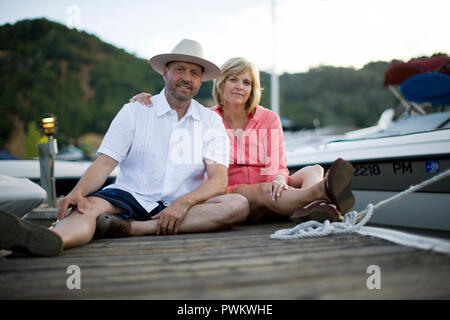 Portrait of a happy couple sitting next to each other on a wooden jetty. Stock Photo