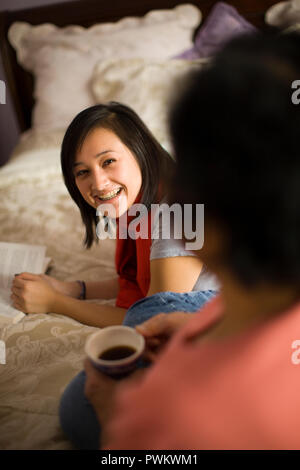 Teenage girl reading in her bedroom and talking to her mom Stock Photo