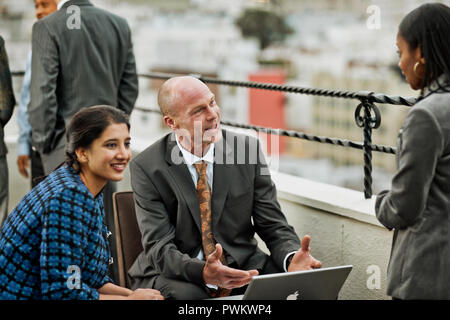 Smiling group of co-workers have a friendly meeting on the balcony of their high-rise building. Stock Photo