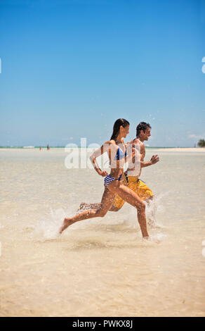 Happy mid adult couple running through shallow water at the beach. Stock Photo