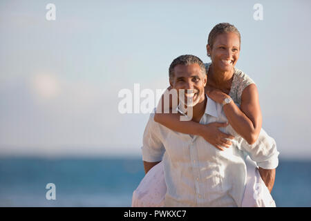 Man giving a piggy back ride to his partner on the beach. Stock Photo