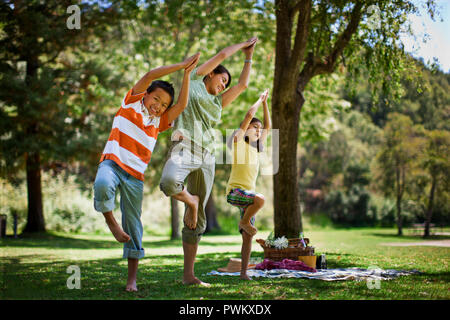 Mother practicing yoga poses with her two children. Stock Photo