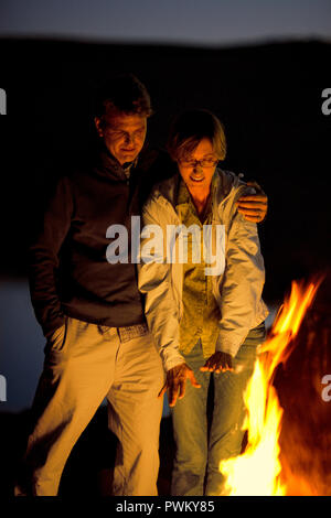 Smiling husband and wife sitting near a bonfire on a beach. Stock Photo