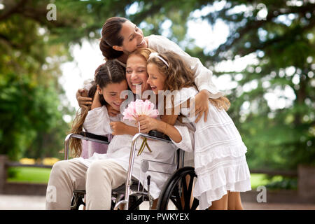 Multi-generational family hugging grandmother in wheelchair. Stock Photo