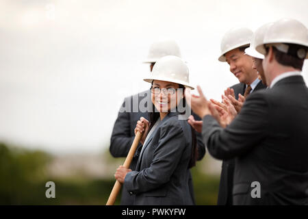 Smiling middle-aged businesswoman performs the groundbreaking ceremony of a new development as her colleagues look on happily and applaud. Stock Photo