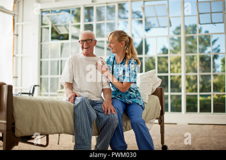 Smiling senior man being comforted by a female nurse inside his bedroom. Stock Photo