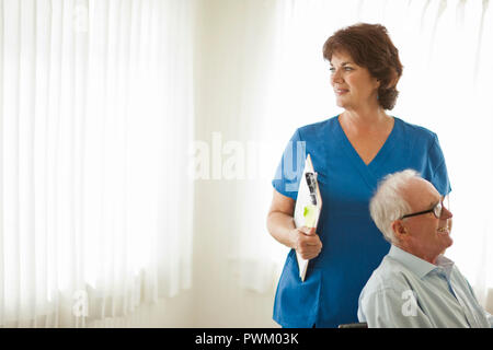 Female nurse next to a senior man sitting in a wheelchair. Stock Photo