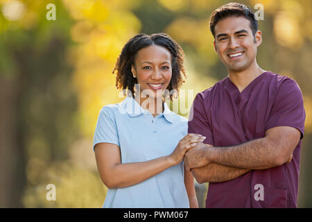 Portrait of a smiling male and female nurse side by side in a park. Stock Photo