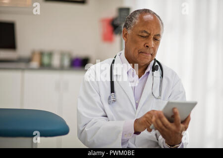 Contemplative male doctor using a digital tablet while sitting inside his office. Stock Photo