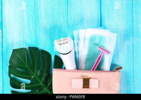 Means for hair removal. Epilator, razor for shaving, wax strips on a tropical leaf on a blue wooden background. Epilation, depilation, shaving Stock Photo
