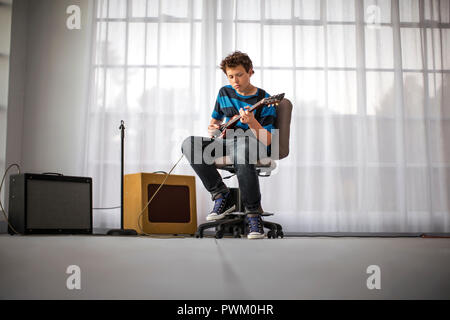 Teenage boy playing electric guitar in living room. Stock Photo