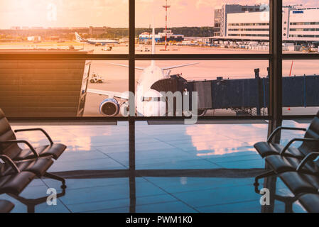 Empty rows of seats in airport waiting area. Chairs in big light hall waiting for passengers to arrive. Trips and travelling. Plane in background Stock Photo