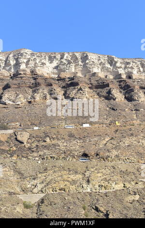 Greece, the island of Santorini.  Towering above the port are the volcanic rock formations of the caldera Stock Photo