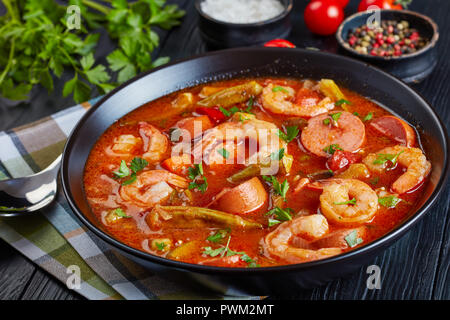 Delicious gumbo with prawns, baby okra and sausage in a bowl on a black table with napkin and silver spoon,  view from above, close-up Stock Photo