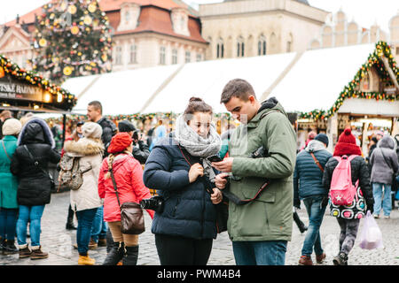 Prague, December 25, 2017: A young couple of tourists looks at a map on a cell phone on the main square in Prague during the Christmas holidays. Stock Photo