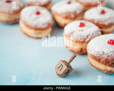 Jewish holiday Hanukkah concept and background. Hanukkah food doughnuts and traditional spinnig dreidl or dredel on blue background. Copy space for text. Shallow DOF Stock Photo