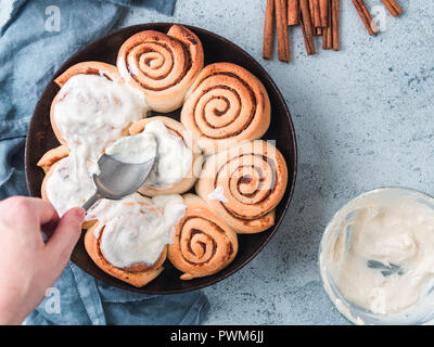 Woman's Hand Spreading Frosting on Cinnamon Rolls in Skillet. Vegan swedish cinnamon buns Kanelbullar with pumpkin spice,topping vegan cream cheese. Top view or flat lay. Copy space for text Stock Photo