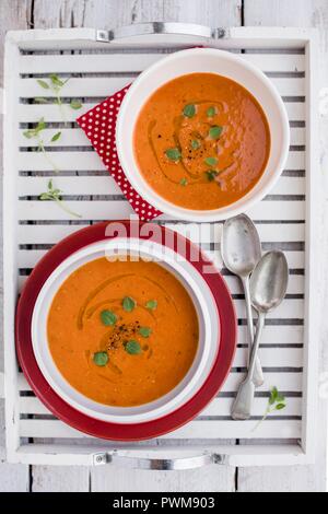Two bowls of cream of tomato soup with fresh basil on a wooden tray Stock Photo