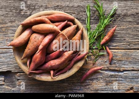 Sweet potatoes in a wooden bowl with sprigs of rosemary Stock Photo