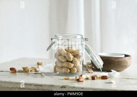 Peanuts in and next to a glass jar on a rustic kitchen table Stock Photo