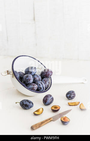 Damsons in a colander with a knife on a light surface Stock Photo