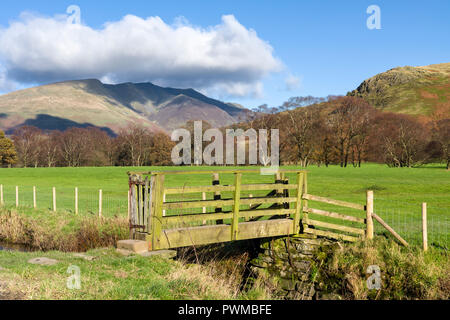 A wooden footbridge over a small beck at Dale Bottom with Blencathra beyond in the English Lake District National Park, Cumbria, England. Stock Photo