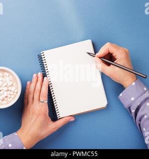 Woman's hand writing in notebook on the blue background. Top view. Stock Photo