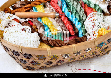 Vintage basket with sewing kit, multi-colored threads on fabric background,hand-knit lace Stock Photo