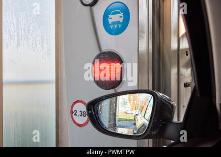 Close-up photo of a rear-view mirror inside a car wash with water drops, a symbol and a red shining STOP sign on a traffic light Stock Photo
