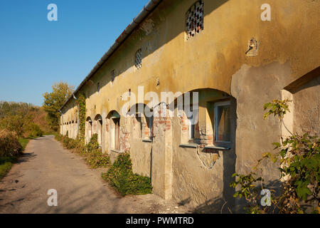 Old cracked building - barracks or farmhouse, asphalt road in the evening sunshine Stock Photo