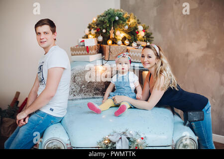 Dad and mom kissing little daughter from sides, posing in decorated for Christmas studio. Stock Photo