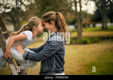 Smiling young mother holds her little girl who is sitting on a ladder. Stock Photo