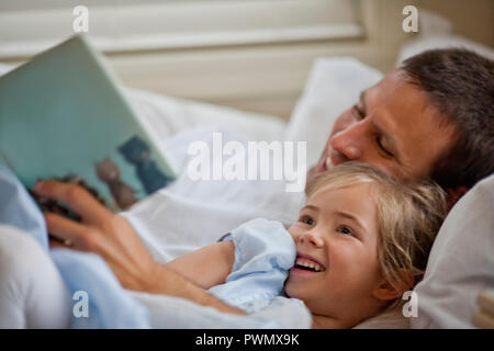 Happy father lying down reading a book with his daughter. Stock Photo