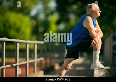 Senior man warming up with stretches on bleachers. Stock Photo